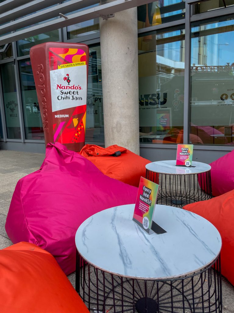 nandos brand activation setting with bean bags, a table, and a giant bottle of chilli jam