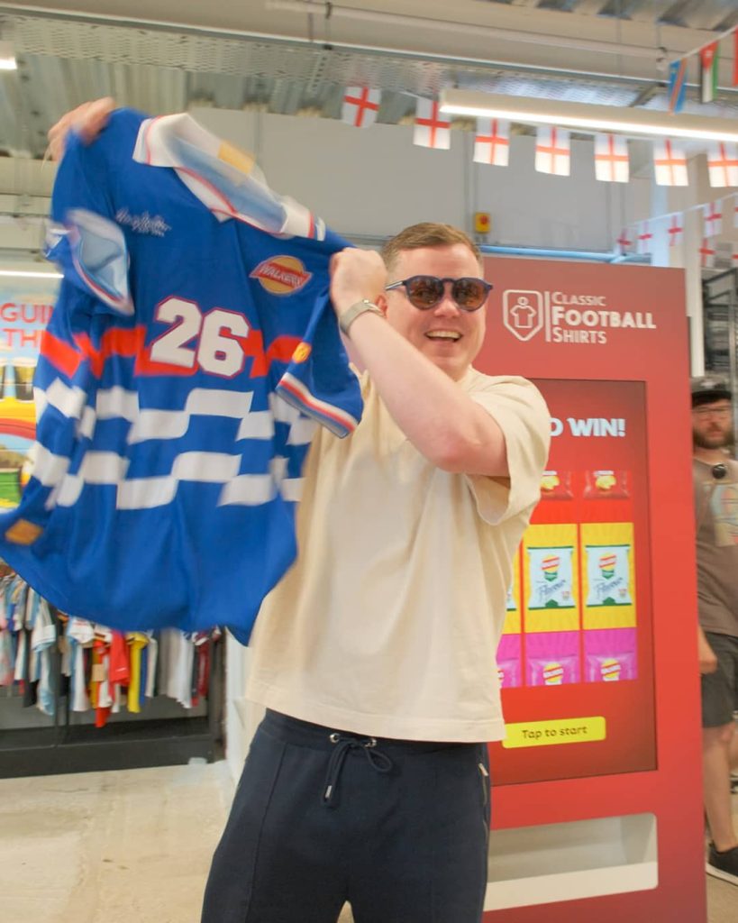 Man showing off limited edition walkers branded football shirt in front of vending machine